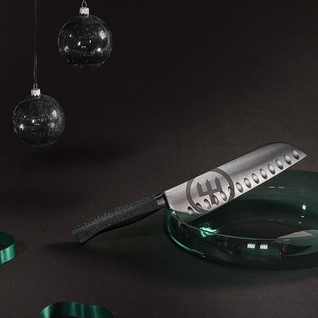 Decorative spatula with a logo on a dark background with Christmas ornaments and ribbons.
