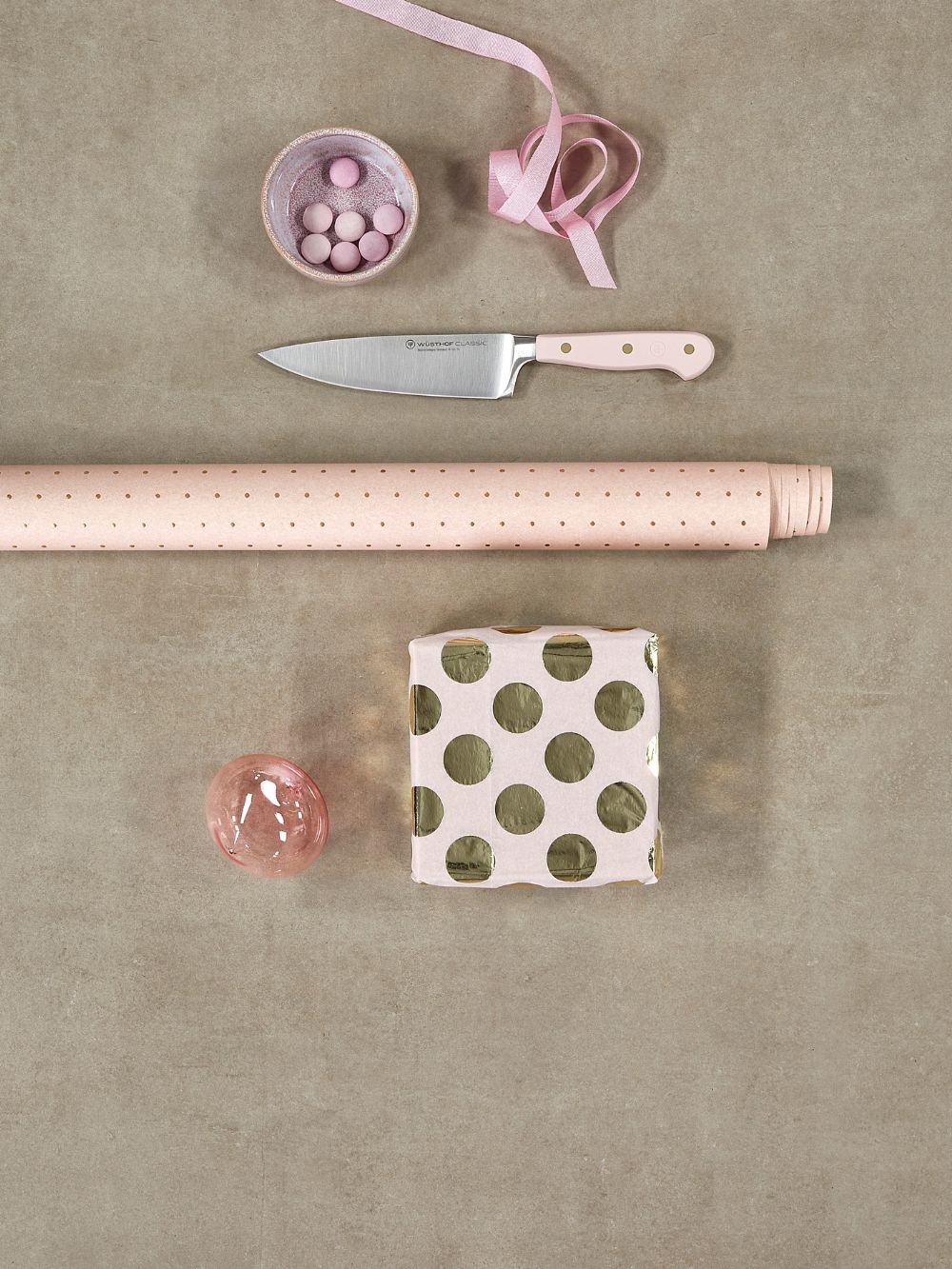 Pink rolling pin, knife, polka dot box, and pink candy on a beige surface