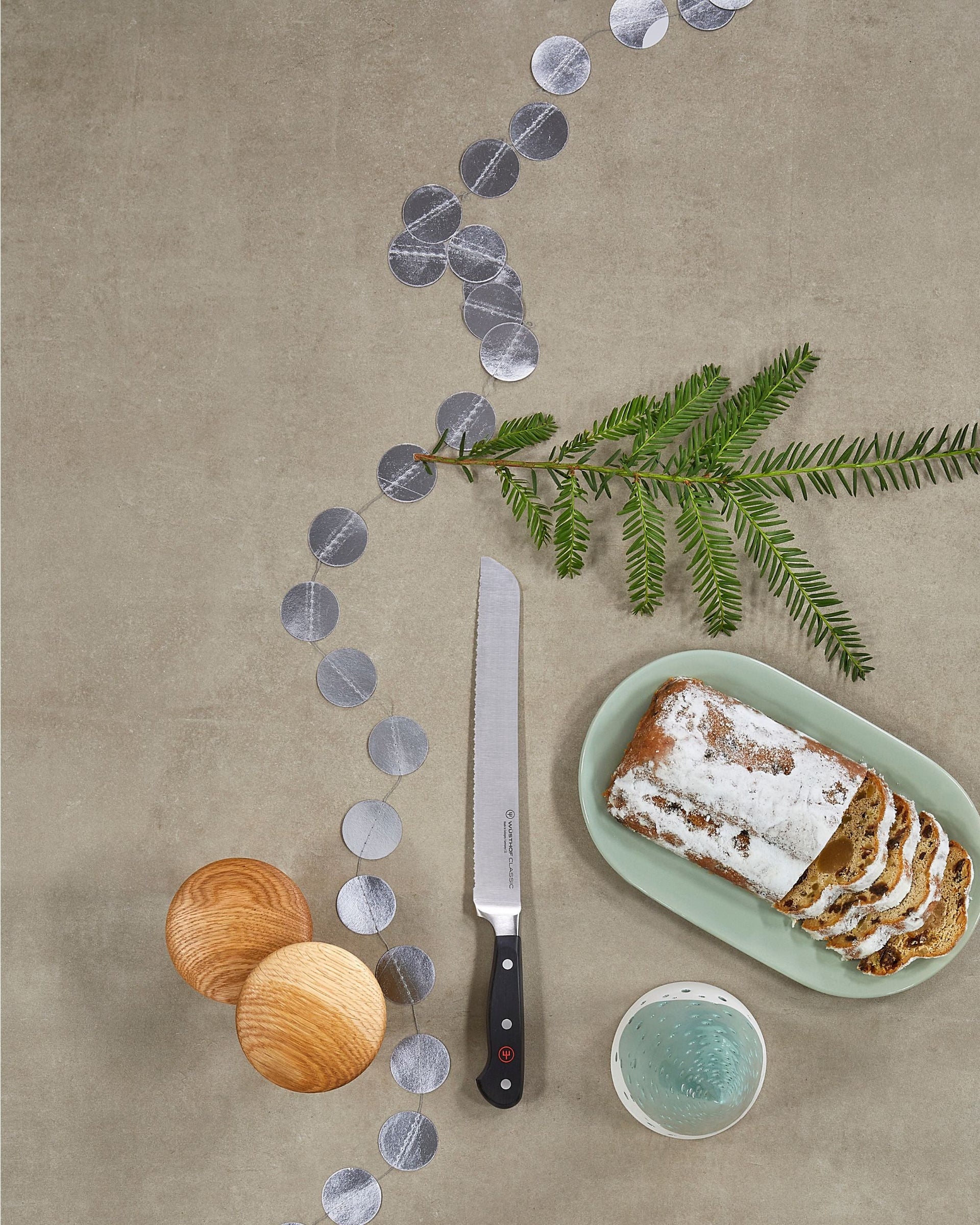 Loaf of bread on a green plate with a knife, decorative elements, and a bowl on a beige surface.