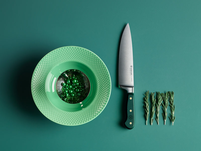 Green plate with a small dish, knife, and sprigs of greenery on a teal background