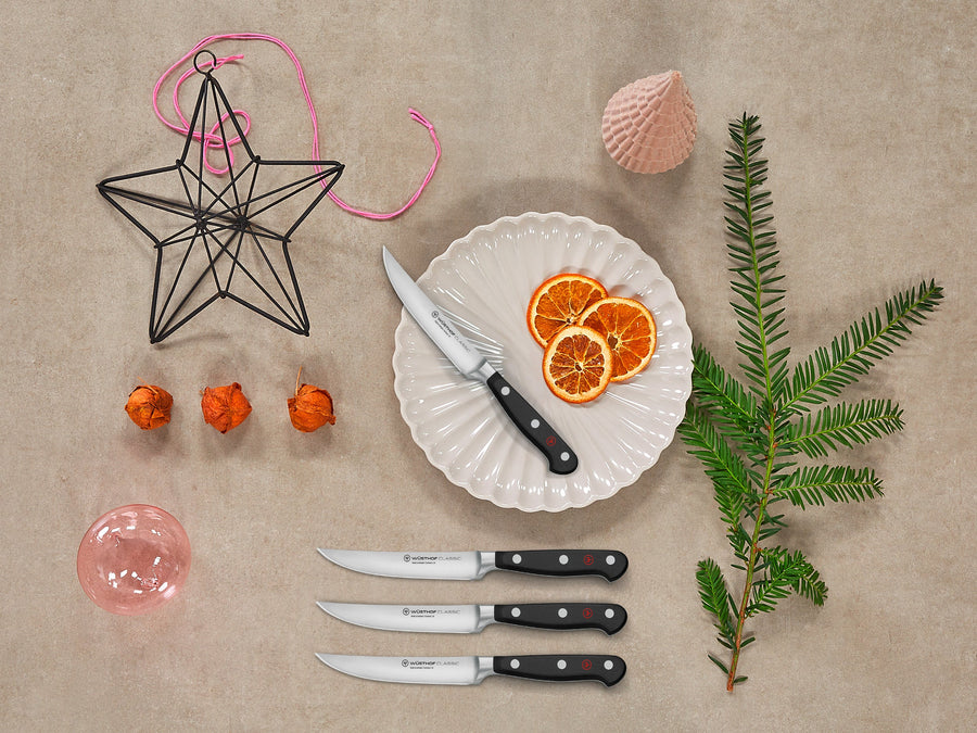 Decorative items including a star-shaped ornament, knives, an orange slice on a plate, and a green branch on a beige background.