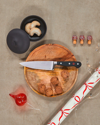 Wooden cutting board with knife, bread, and decorative items on a beige surface