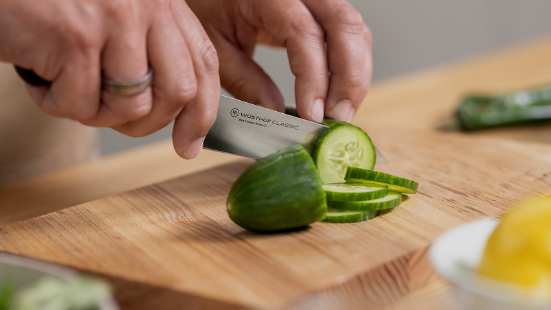 Person slicing a cucumber on a wooden cutting board with a Wusthof knife.