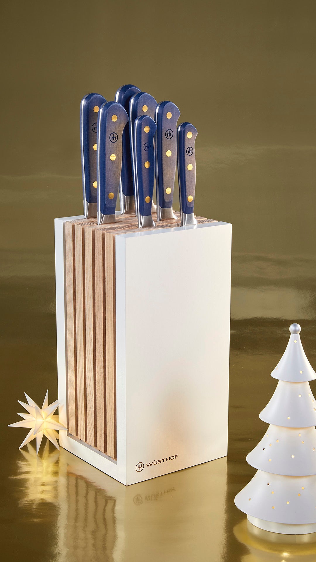 Set of knives with blue handles in a wooden block on a reflective surface with decorative elements.