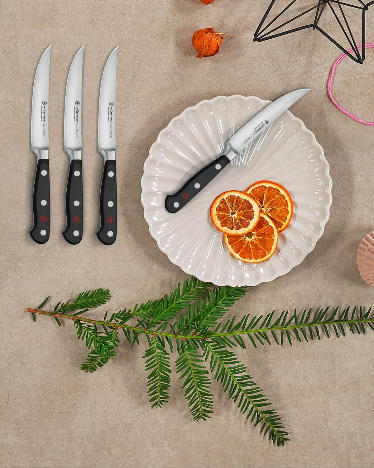 Set of knives on a beige surface with a plate of sliced oranges and a branch of greenery.