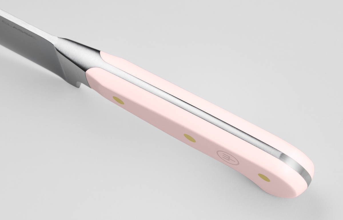Close-up of a light pink knife handle with three brass rivets, showcasing a full tang design and subtle embossed logo on a sleek German chef knife.