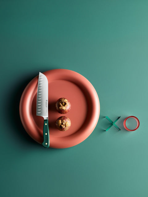 A knife and two halved apples on a red plate against a green background, with a red circle and green X beside it.