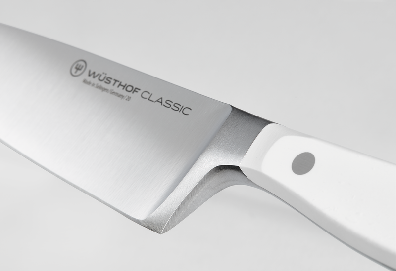 Close-up of a polished steel blade with a full bolster and a white ergonomic handle featuring a single rivet for balanced grip.